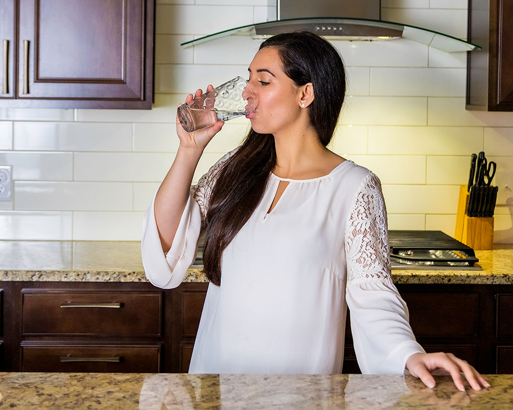 Woman drinking a glass of purified water in a kitchen